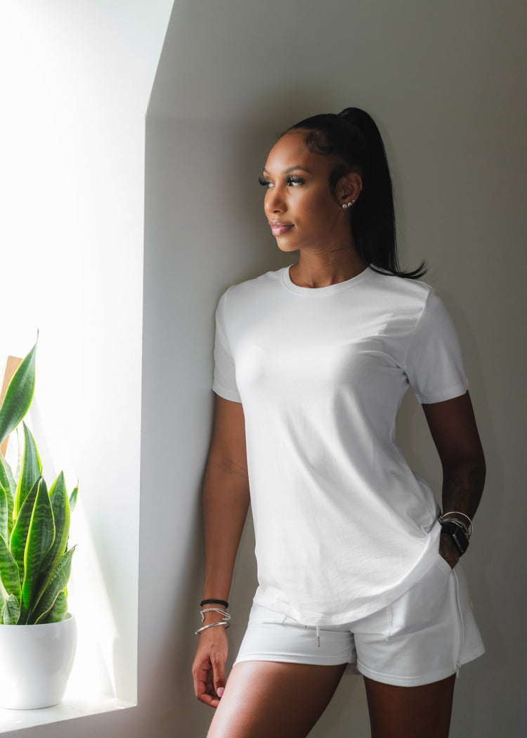 A woman of thirties looking at the window with a white basic round neck t-shirt and a white short